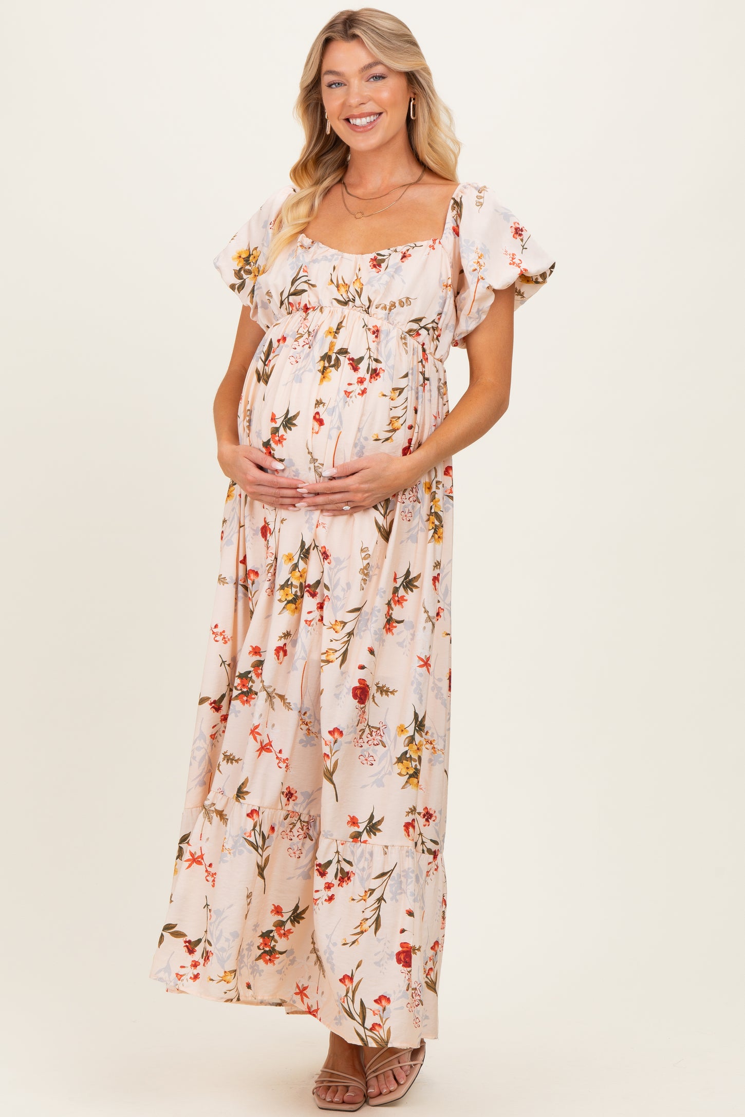 woman wearing a floral print maternity maxi dress with flutter sleeves and holding her baby bump