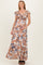 woman wearing a brown floral maternity maxi dress, holding her baby bump with a smile