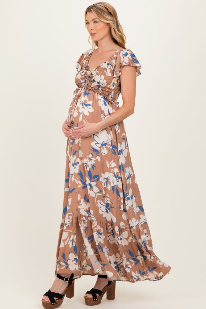 woman wearing a brown floral maternity maxi dress with ruffle sleeves and a baby bump, standing with hands on her belly
