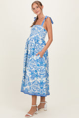 woman wearing a blue and white floral print maternity dress with tie straps and pockets, showcasing her baby bump