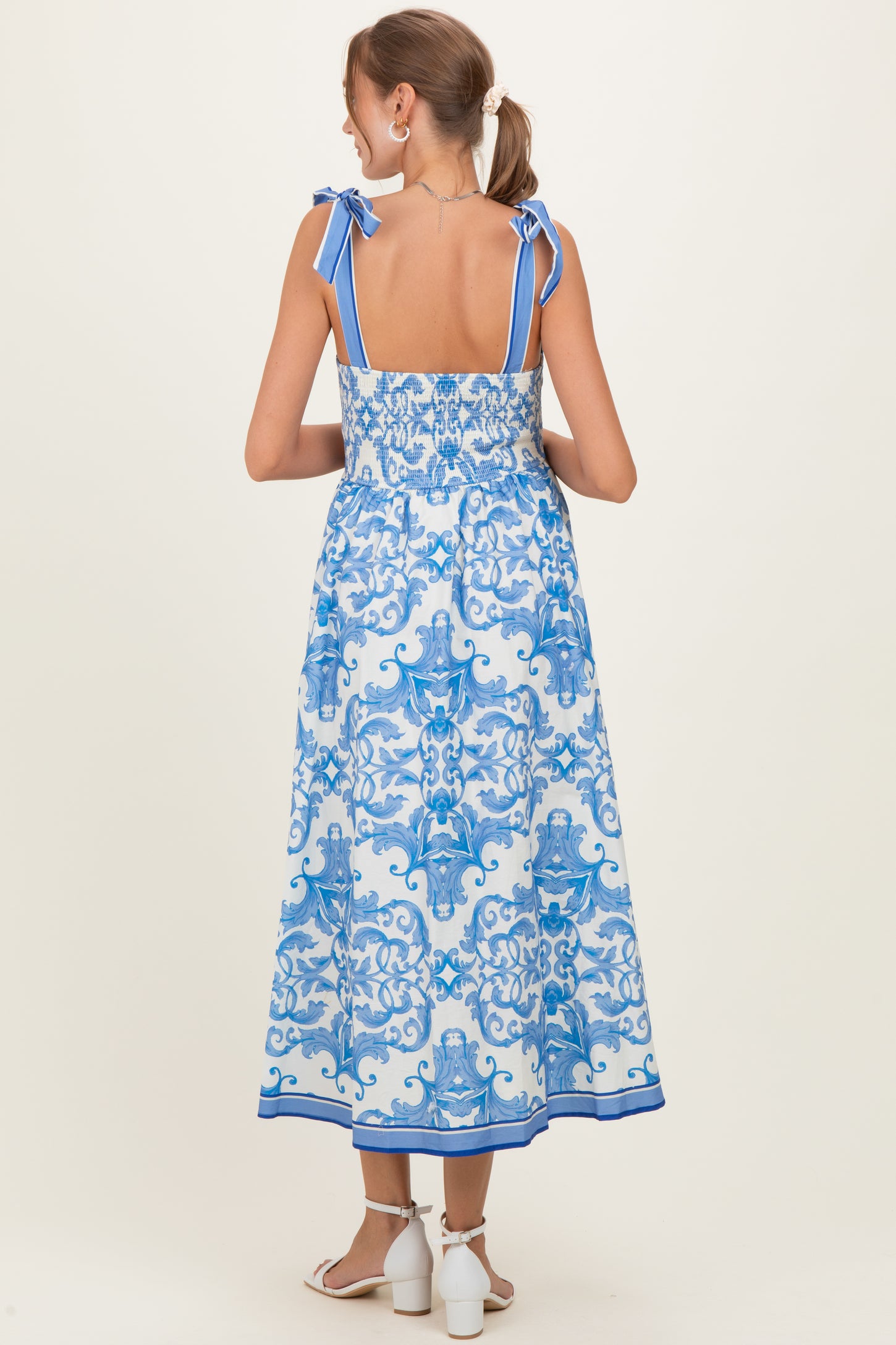 woman wearing a blue and white patterned maternity dress with ribbon straps, showing her pregnant belly from the back