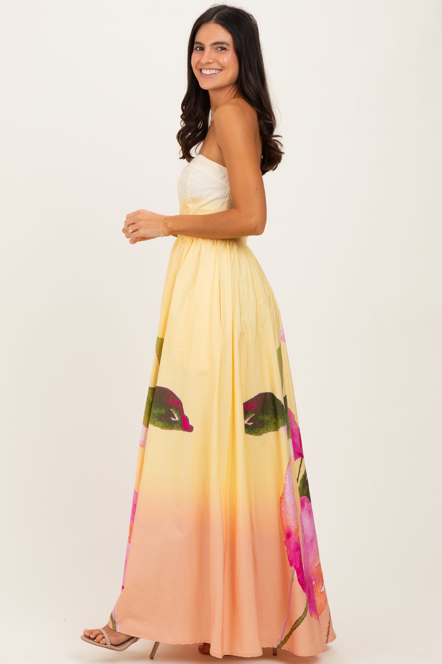 woman wearing a yellow and pink floral maxi dress with a strapless design and a flowy skirt