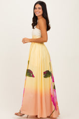 woman wearing a yellow and pink floral maxi dress with a strapless design and a flowy skirt