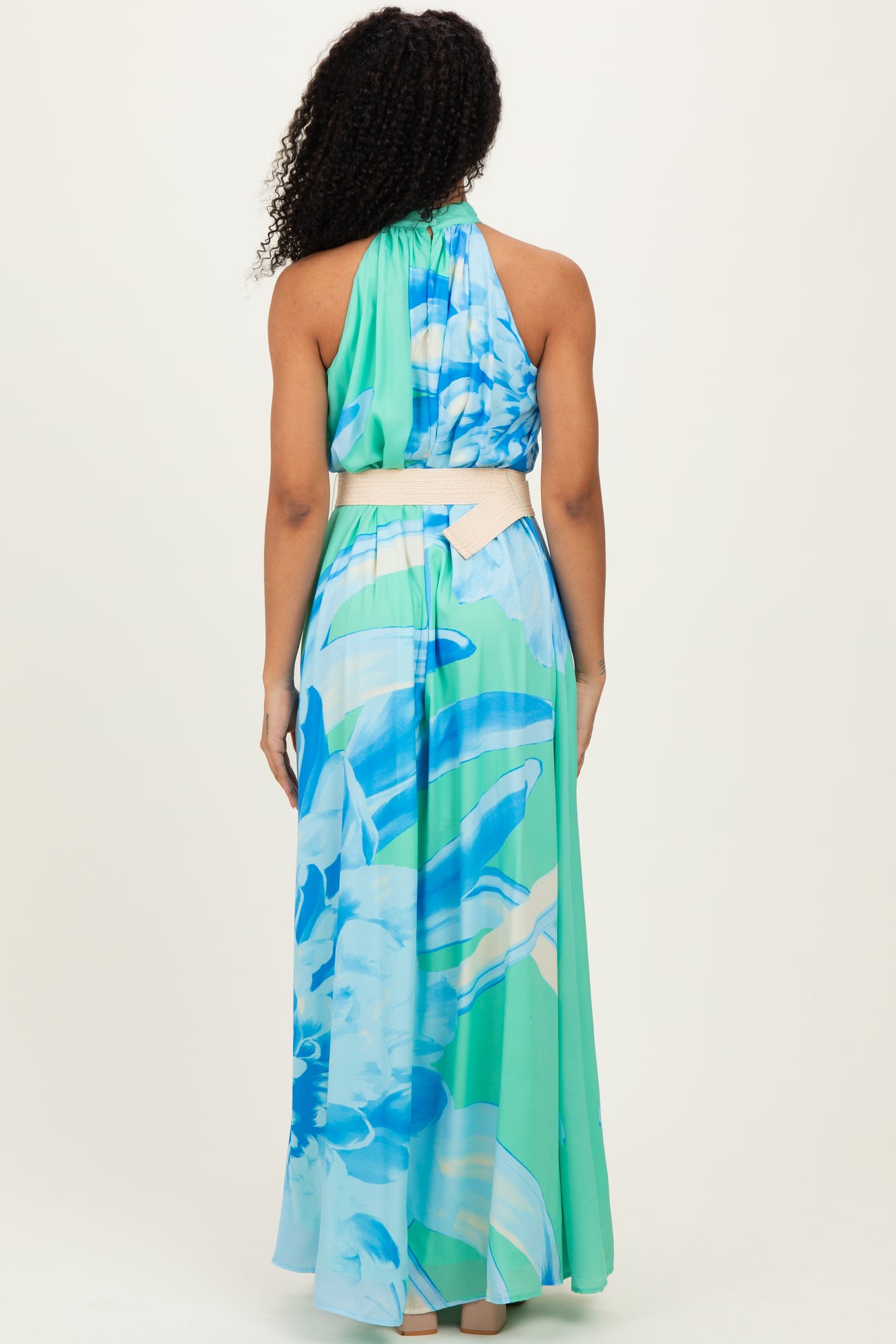 woman wearing a colorful floral halter neck maxi dress with a tie belt, showing the back view