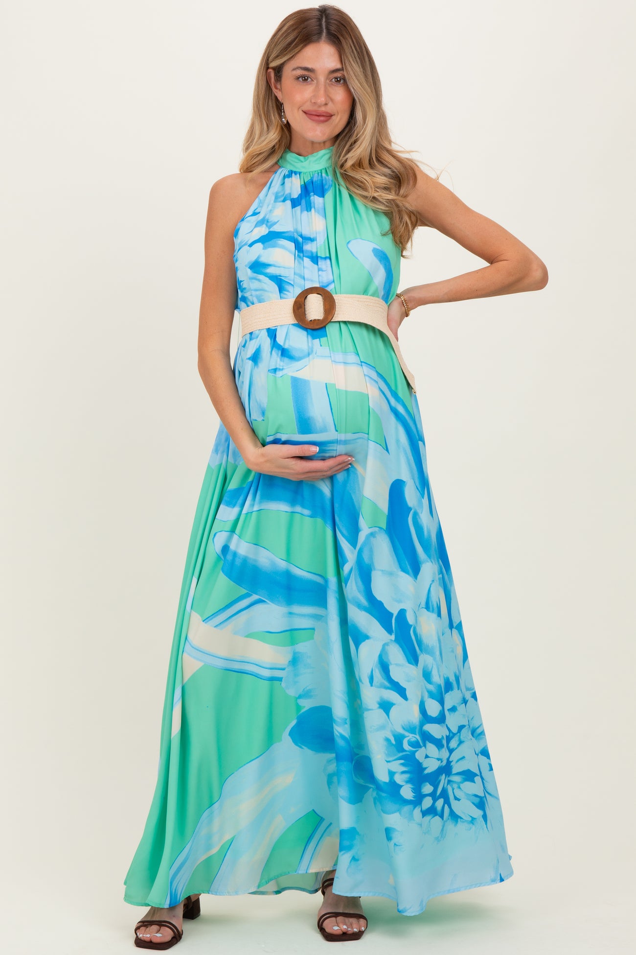 woman wearing a blue and green floral maternity maxi dress, holding her baby bump and styled with a belted waist