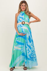 woman wearing a blue and green floral maternity maxi dress, holding her baby bump and styled with a belted waist
