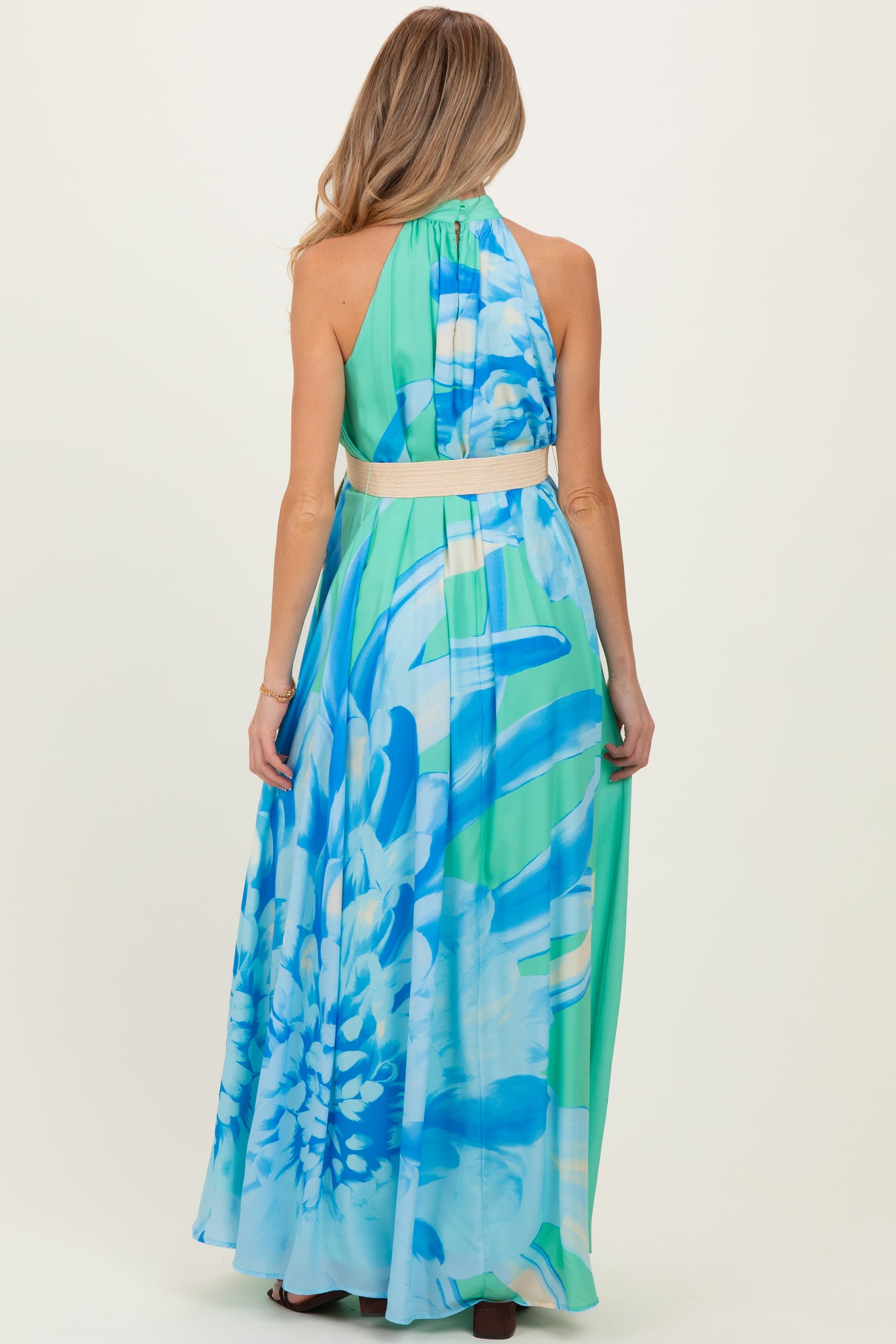 woman wearing a long pastel floral print maternity maxi dress with a halter neck and a wide waistband, showing a baby bump