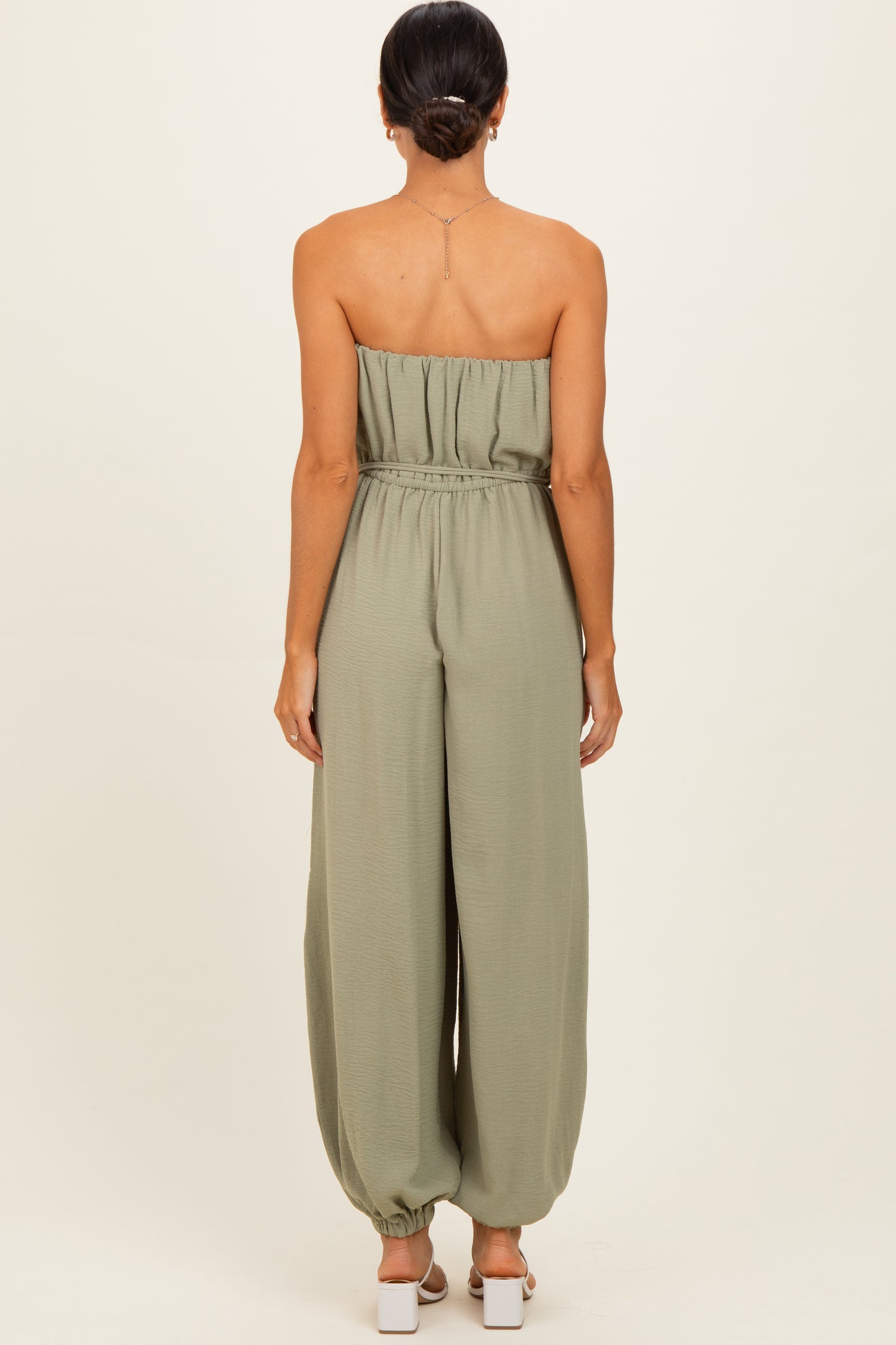 woman wearing astrapless olive green jumpsuit with a loose fit and elastic waistband, viewed from the back
