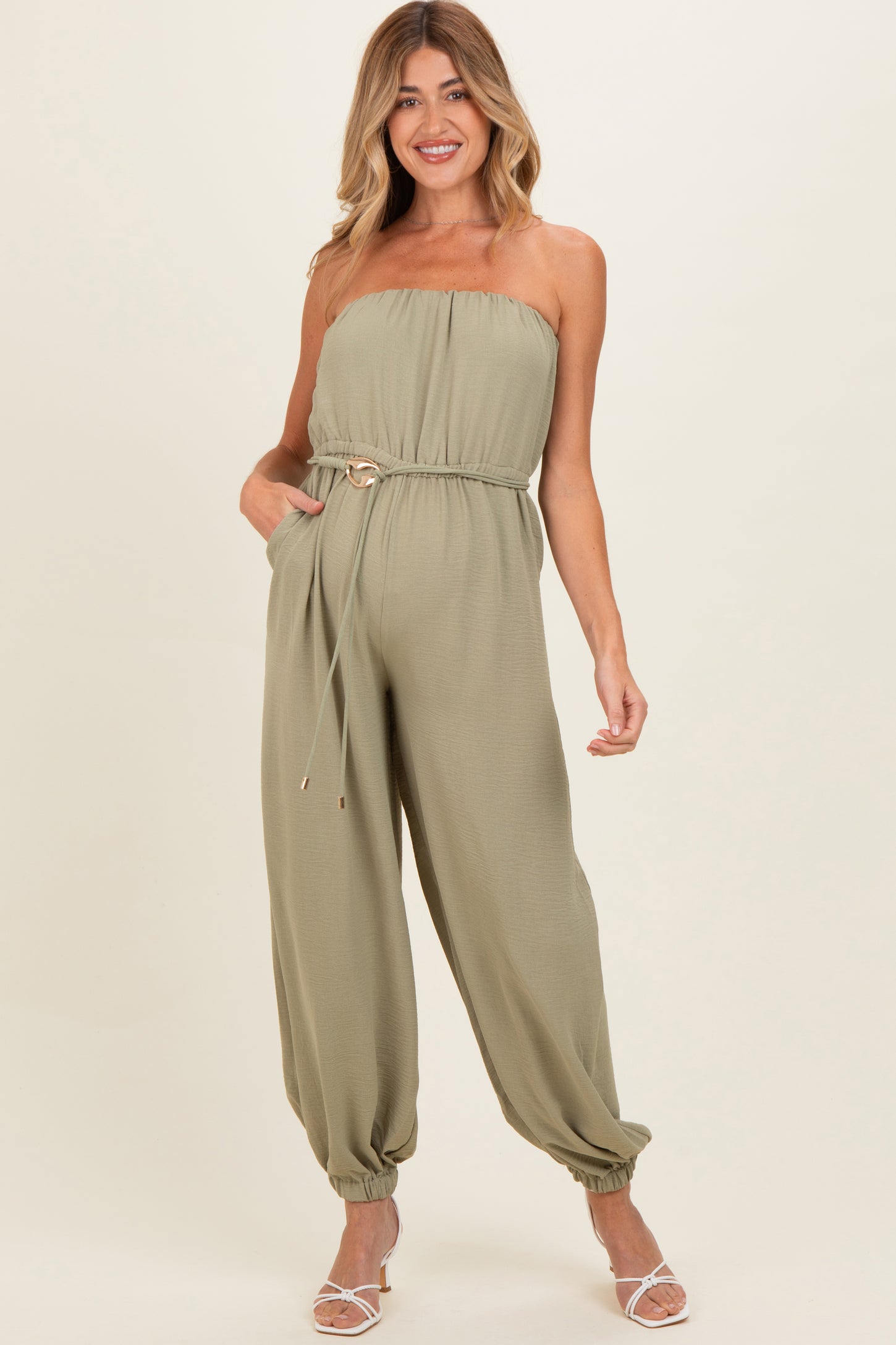 woman wearing a strapless olive green maternity jumpsuit with a drawstring waist and gathered ankle cuffs, showcasing a baby bump