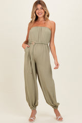woman wearing a strapless olive green maternity jumpsuit with a drawstring waist and gathered ankle cuffs, showcasing a baby bump