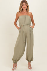woman wearing a green strapless maternity jumpsuit with a belted waist and side pockets, showing a baby bump