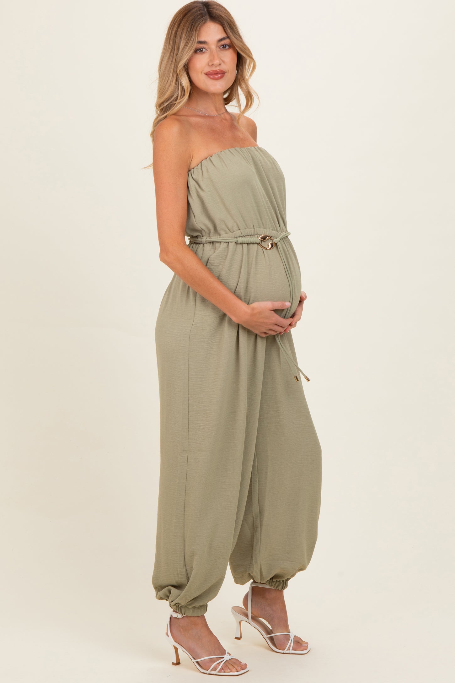 woman wearing a sage green strapless maternity jumpsuit with a drawstring waist and holding her baby bump