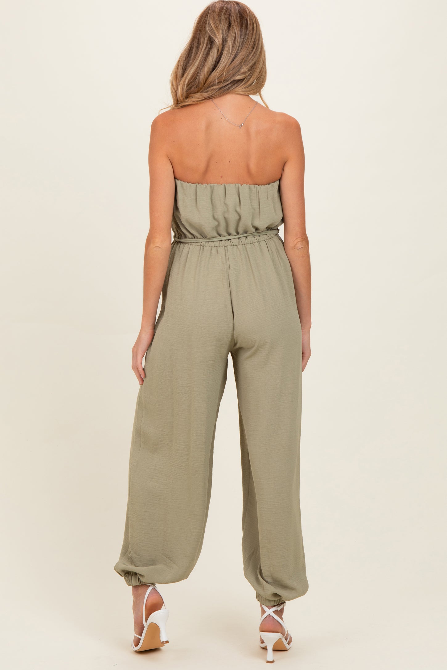 woman wearing a sage green strapless maternity jumpsuit with a fitted waist and wide leg style from the back