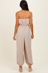 woman wearing a strapless beige jumpsuit with a gathered waistband and relaxed fit, showing the back view