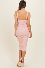 woman wearing a light pink ribbed maternity dress with adjustable straps, showing a fitted silhouette from the back