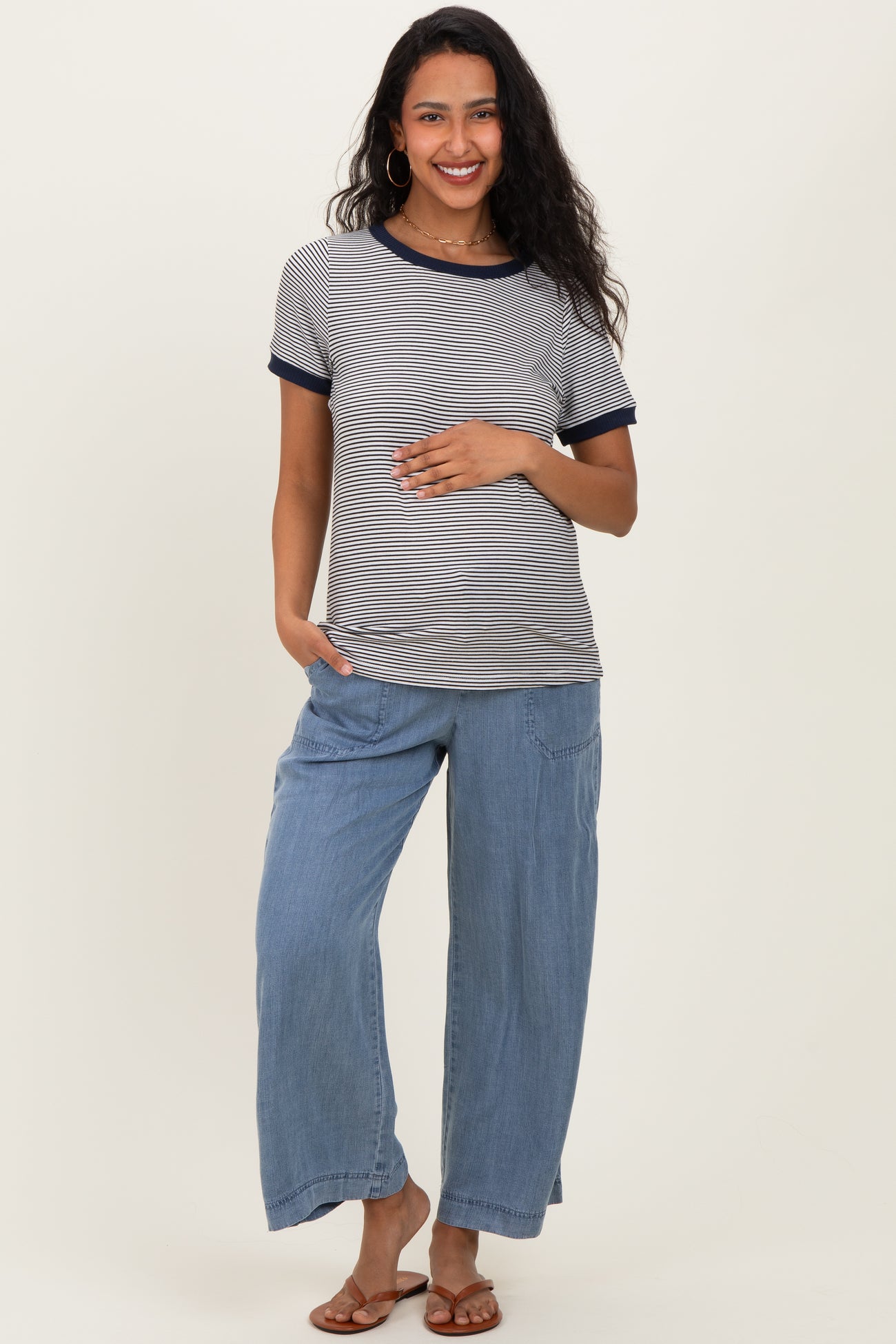 woman wearing a striped maternity top with navy trim and loose blue maternity pants, holding her baby bump