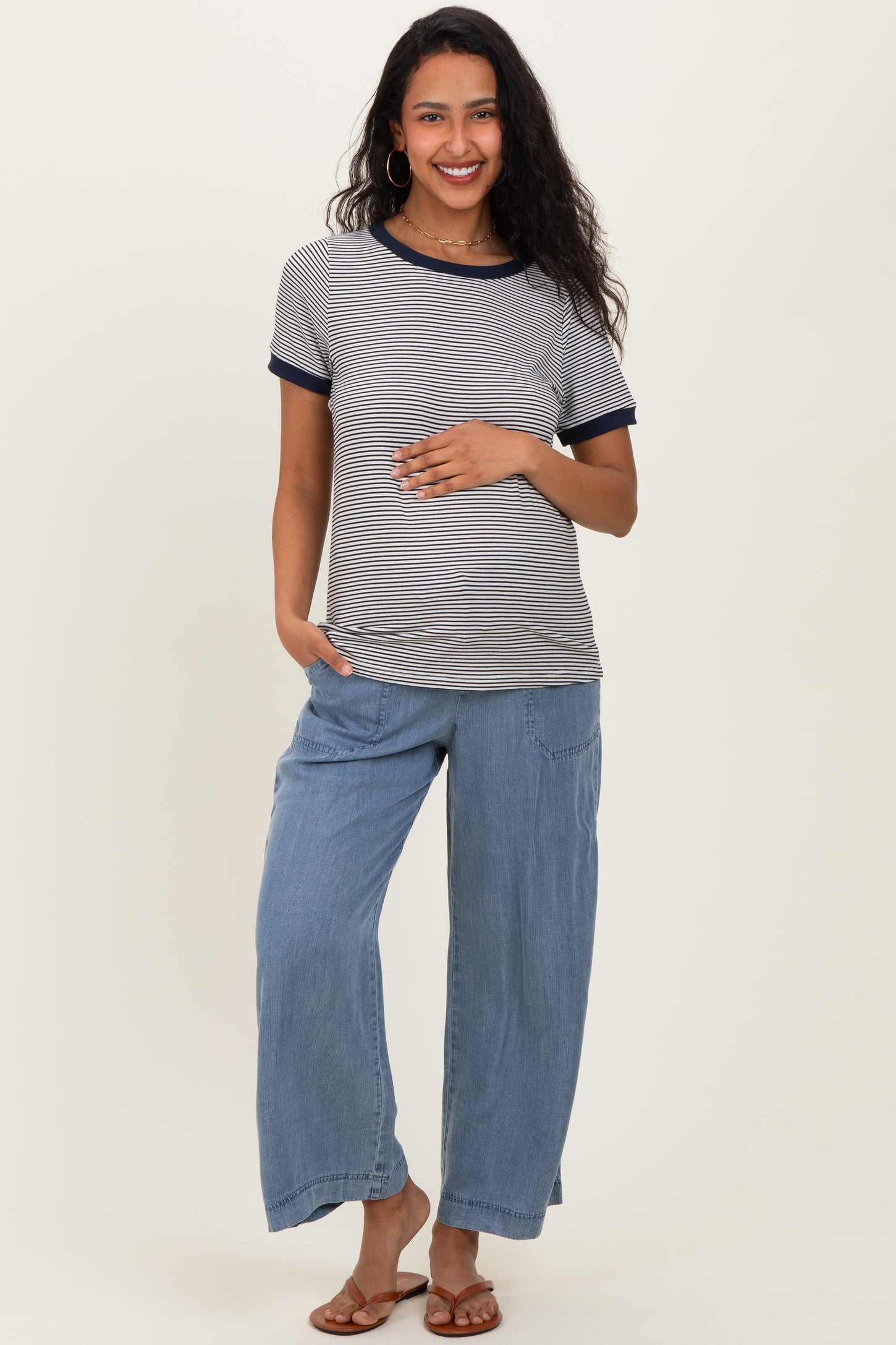 woman wearing a striped maternity top with navy trim and loose blue maternity pants, holding her baby bump