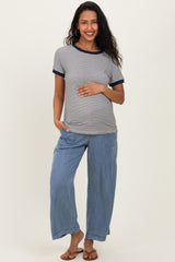 woman wearing a striped maternity top with navy trim and loose blue maternity pants, holding her baby bump