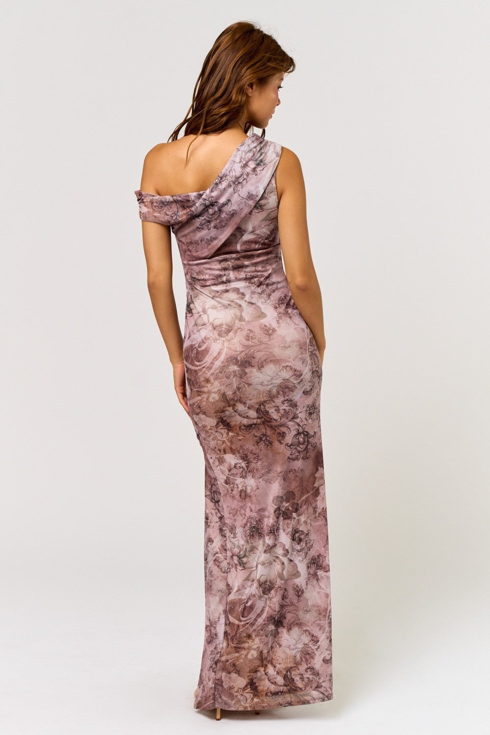 woman wearing a one-shoulder floral maxi dress in shades of pink and beige, showing a fitted silhouette from the back