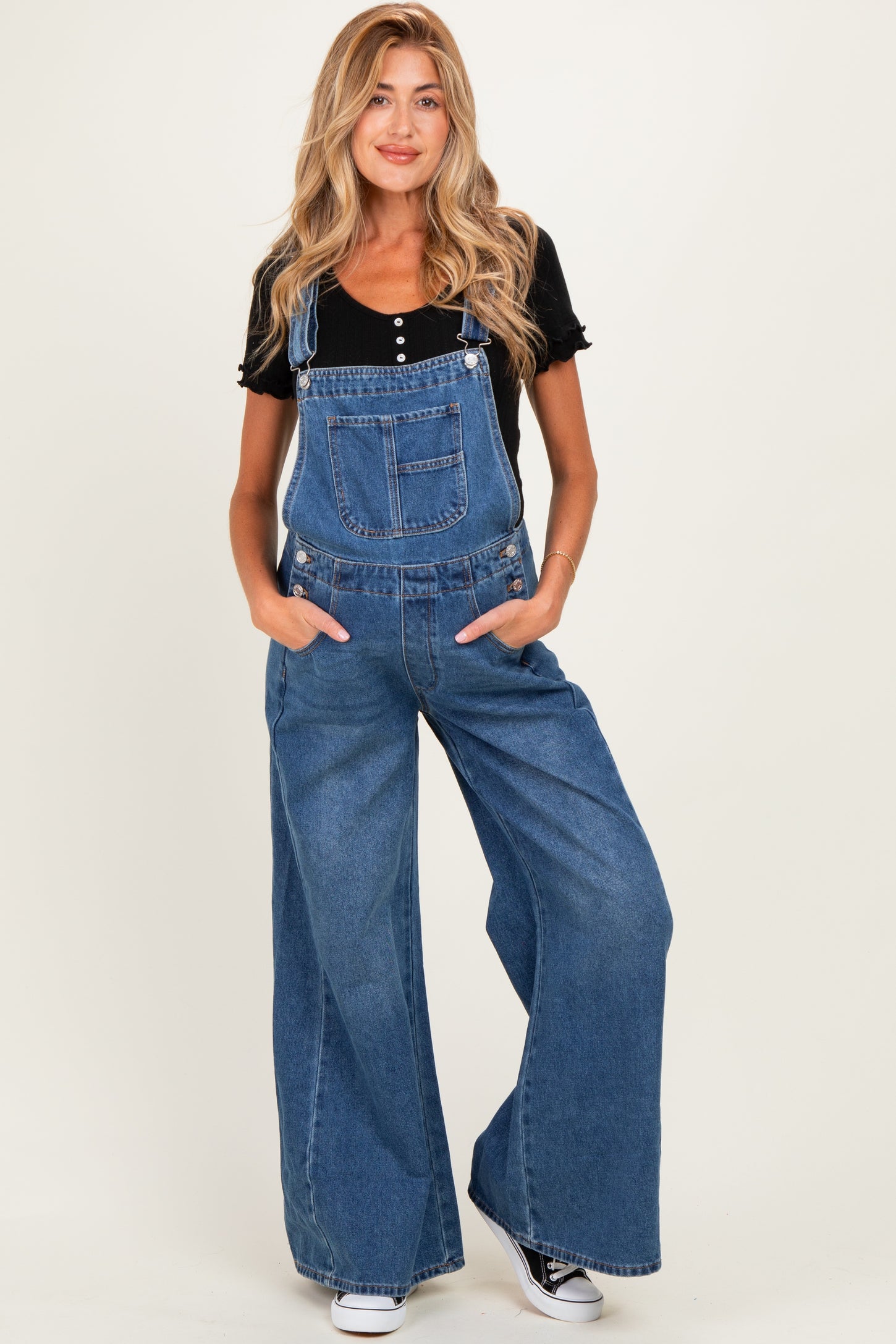 woman wearing a dark blue denim maternity overall jumpsuit with wide legs and a black short sleeve top, no baby bump visible