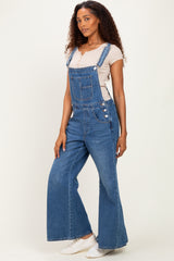 woman wearing a light beige short sleeve top and blue denim overalls with wide legs and side button detailing