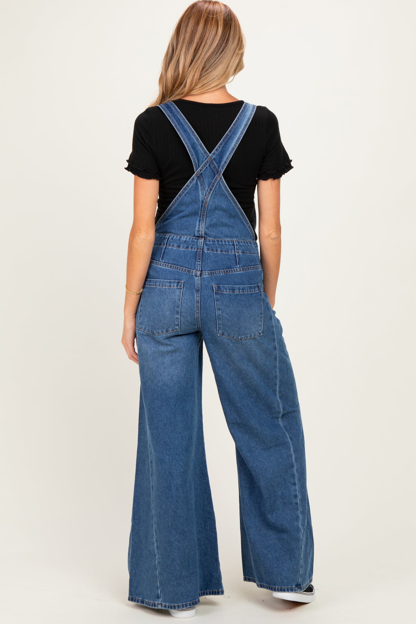 woman wearing a black ruffled short sleeve top and blue denim maternity overalls from the back