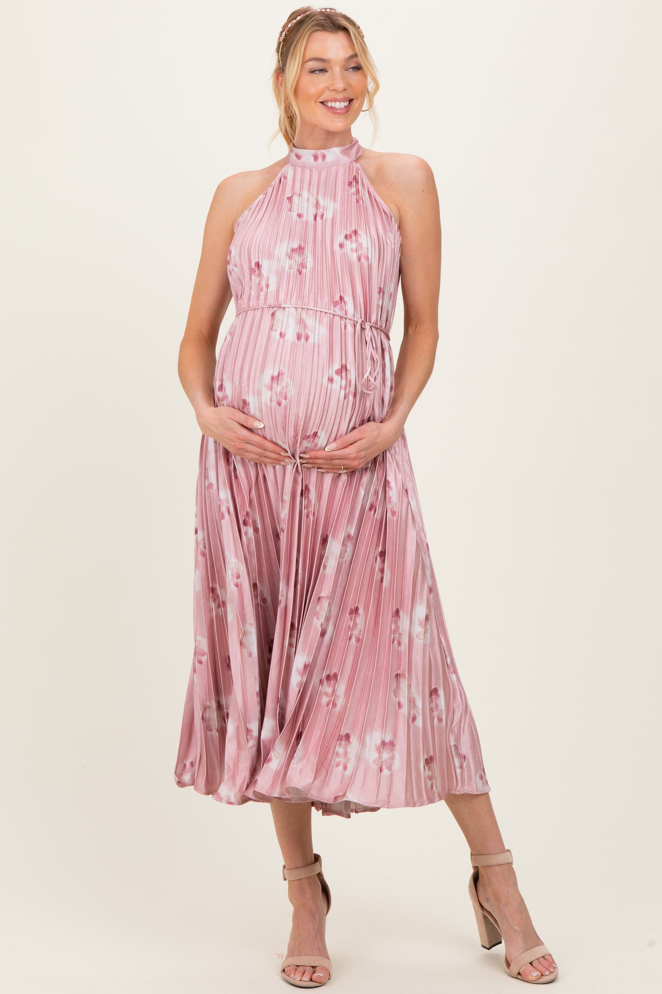 woman wearing a pink floral maternity dress with pleats and a halter neck, showing her baby bump