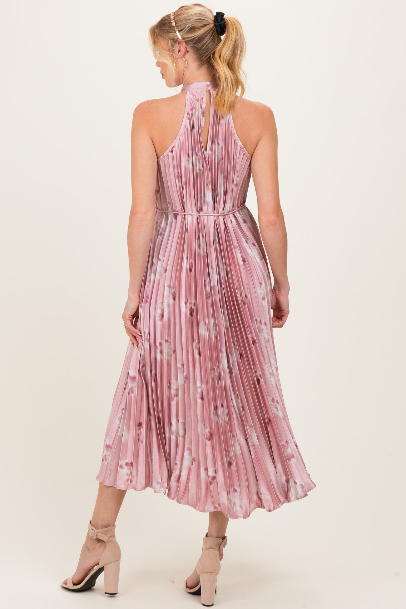 woman wearing a pink floral pleated maternity dress with a halter neckline and a flowing midi skirt