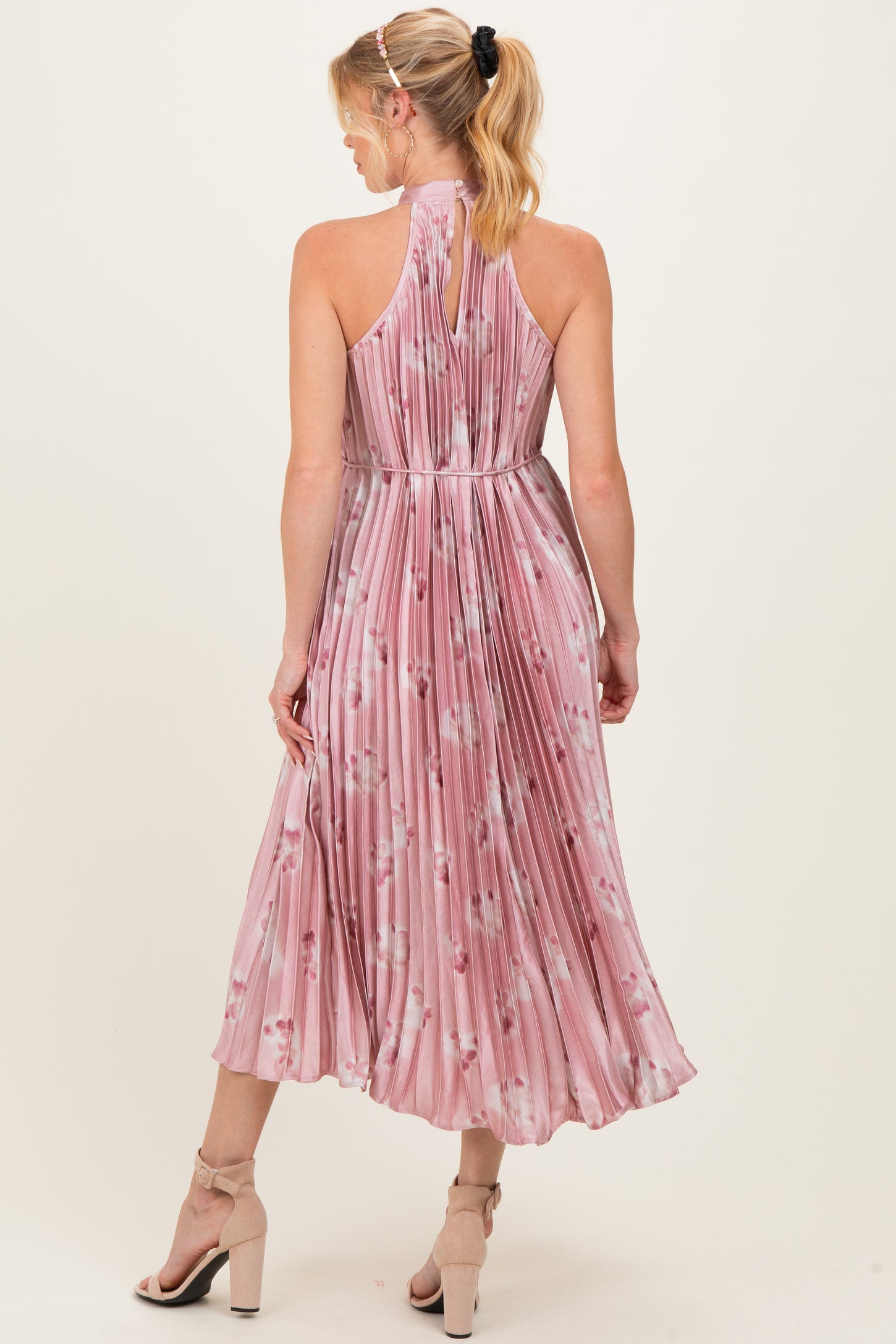 woman wearing a pink floral pleated maternity dress with a halter neckline and a flowing midi skirt