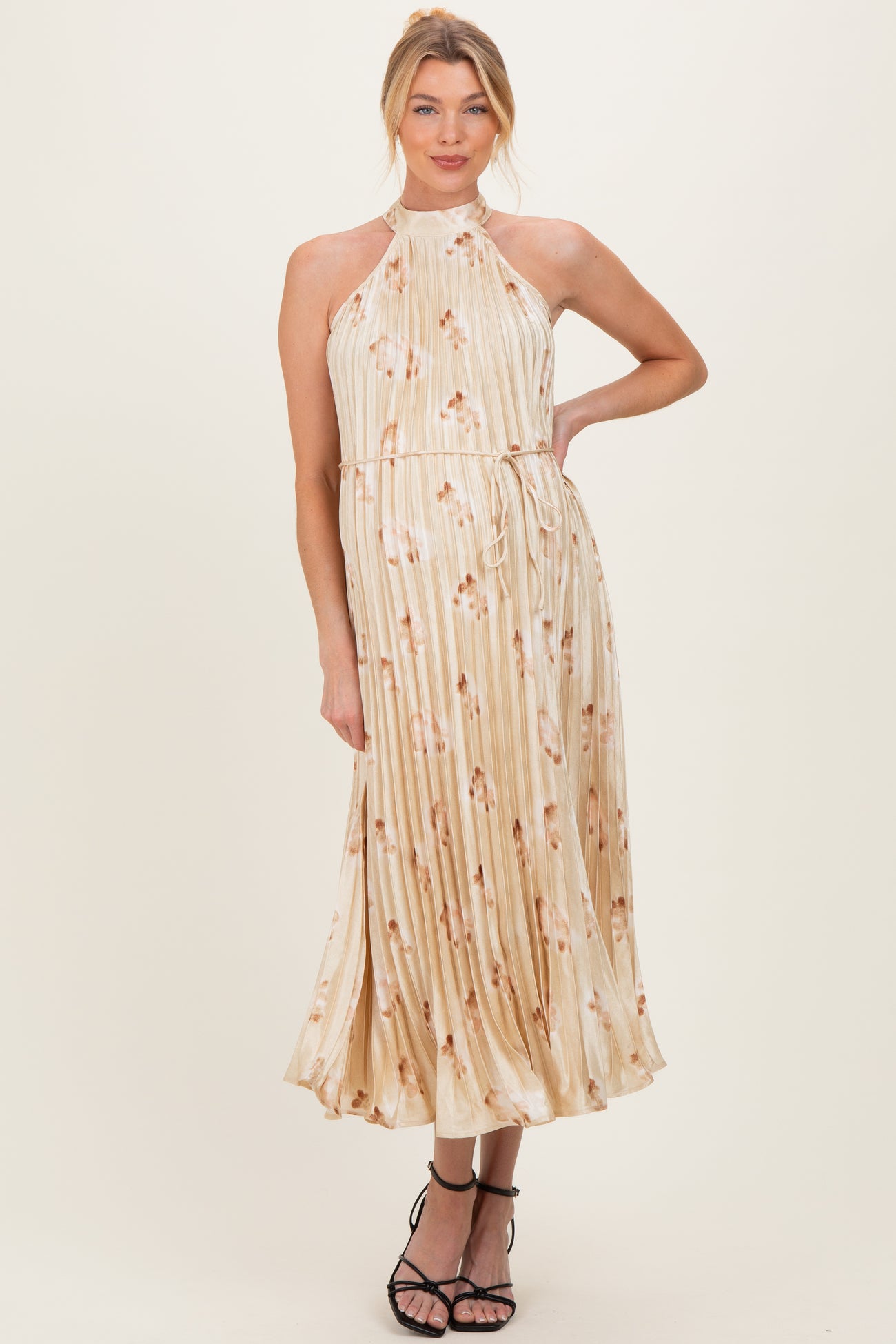 woman wearing a cream floral pleated maternity dress with a halter neck and cinched waist, showing a baby bump