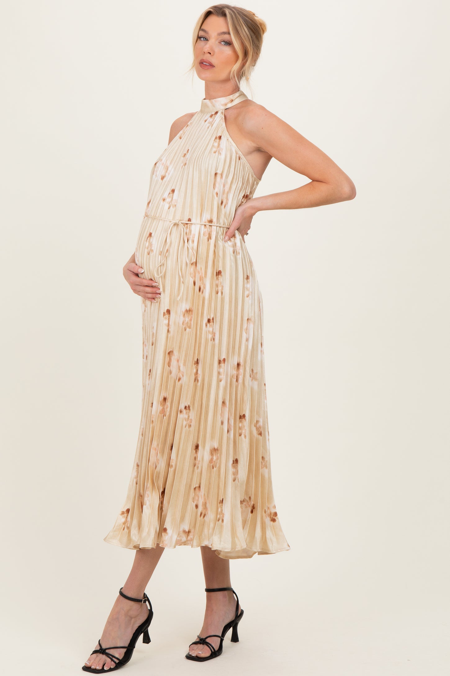 woman wearing a cream floral maternity dress with a halter neck and pleated skirt, revealing her baby bump
