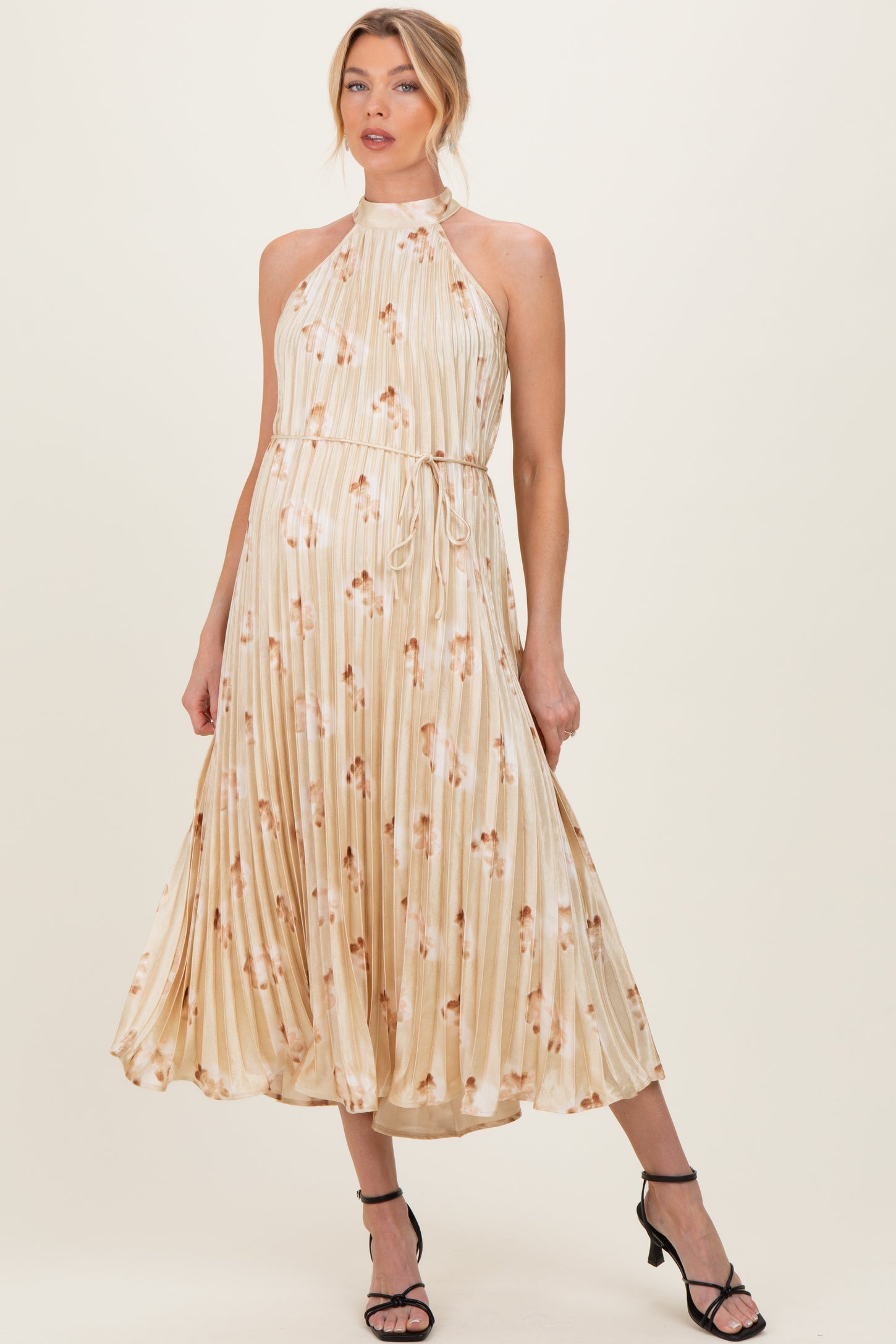 woman wearing a beige floral print maternity dress with a halter neck and a tie belt, showcasing her baby bump