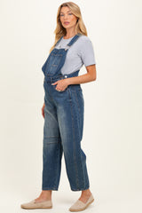 woman wearing a light blue maternity denim overalls with a grey t-shirt underneath and casual slip-on shoes