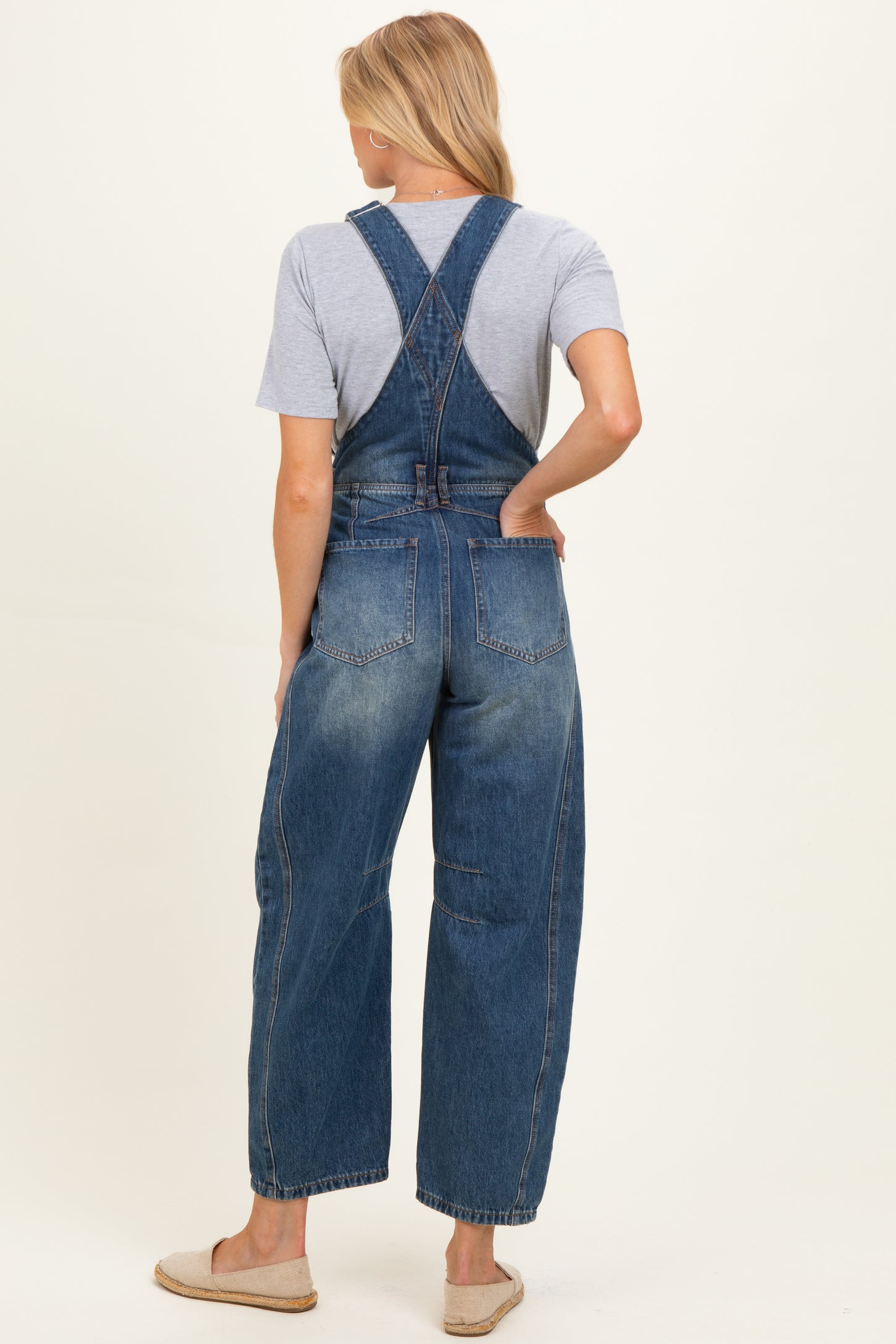 woman wearing a dark wash denim maternity overall with a loose fit and crossed back straps, showing a casual style