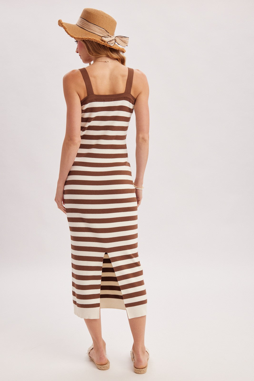 woman wearing a brown and cream striped midi dress with a back slit and a straw hat, facing away from the camera