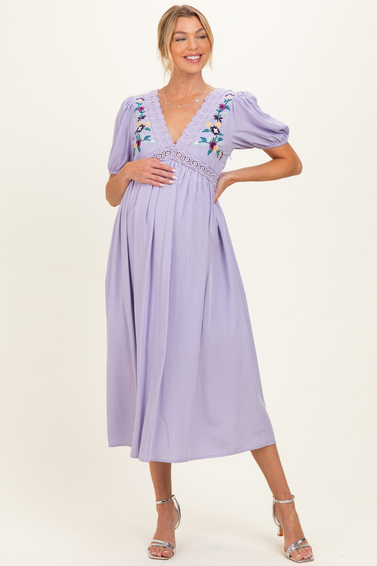 woman wearing a lavender maternity dress with floral embroidery and puff sleeves, holding her baby bump