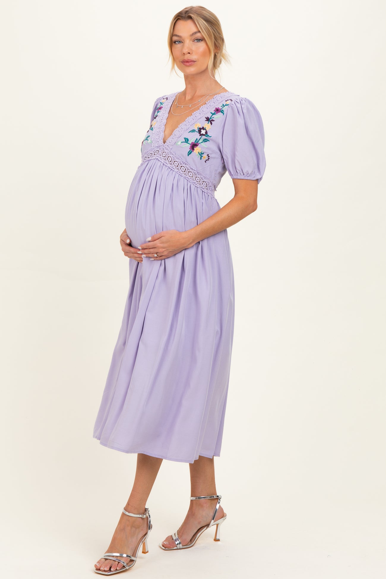 woman wearing a lavender maternity dress with floral embroidery and puff sleeves, holding her baby bump