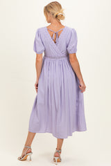 woman wearing a lavender maternity dress with lace details and a tie-back, showcasing a flowing skirt and puff sleeves