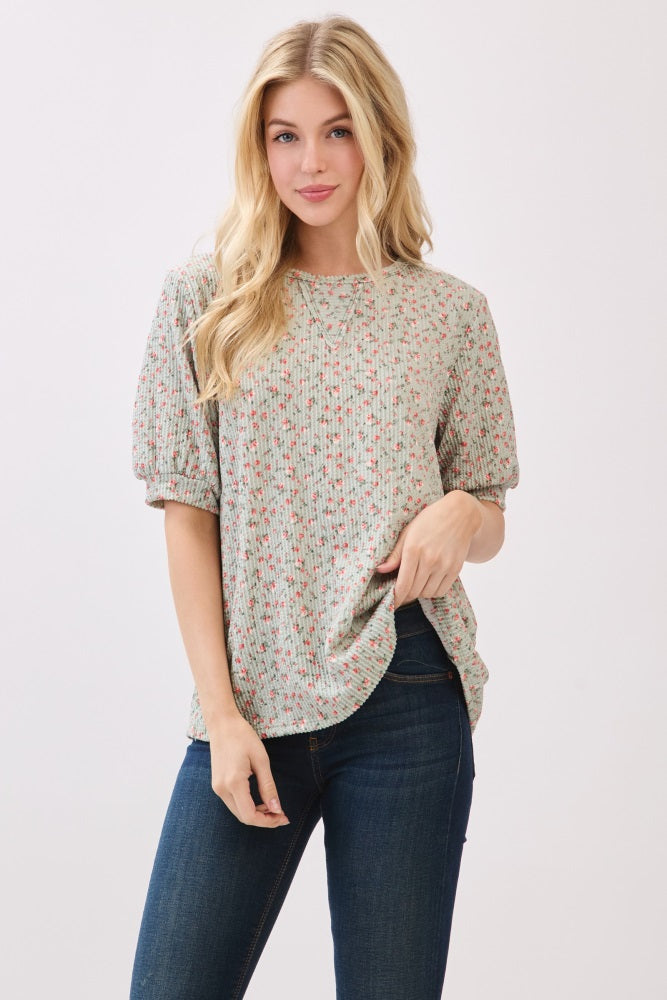 woman wearing a green floral puff sleeve top with a round neckline and light blue jeans