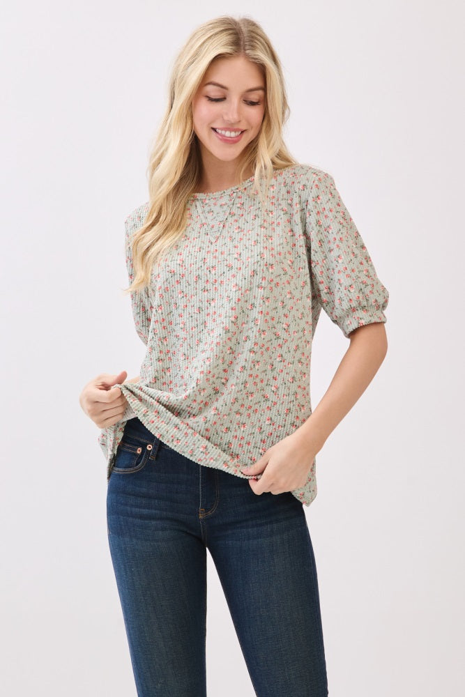 woman wearing a light green floral print blouse with puff sleeves and holding the hem, paired with dark blue jeans