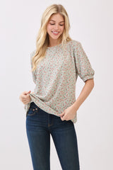 woman wearing a light green floral print blouse with puff sleeves and holding the hem, paired with dark blue jeans