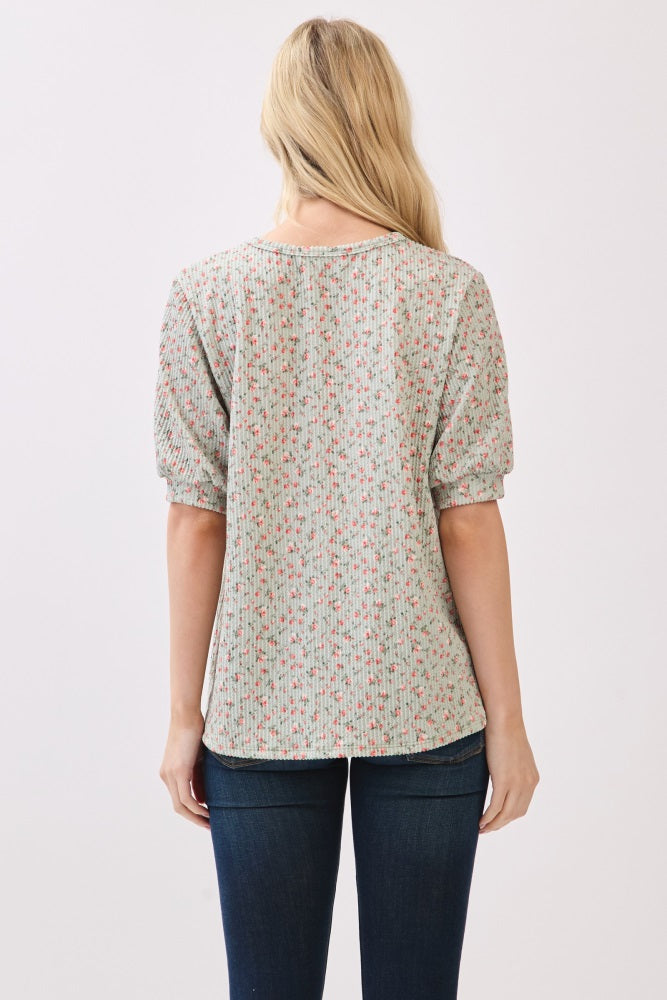 woman wearing a light green puff sleeve top with a floral print and blue jeans, viewed from the back