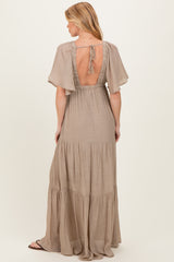 woman wearing a beige maternity maxi dress with short flutter sleeves and open back design