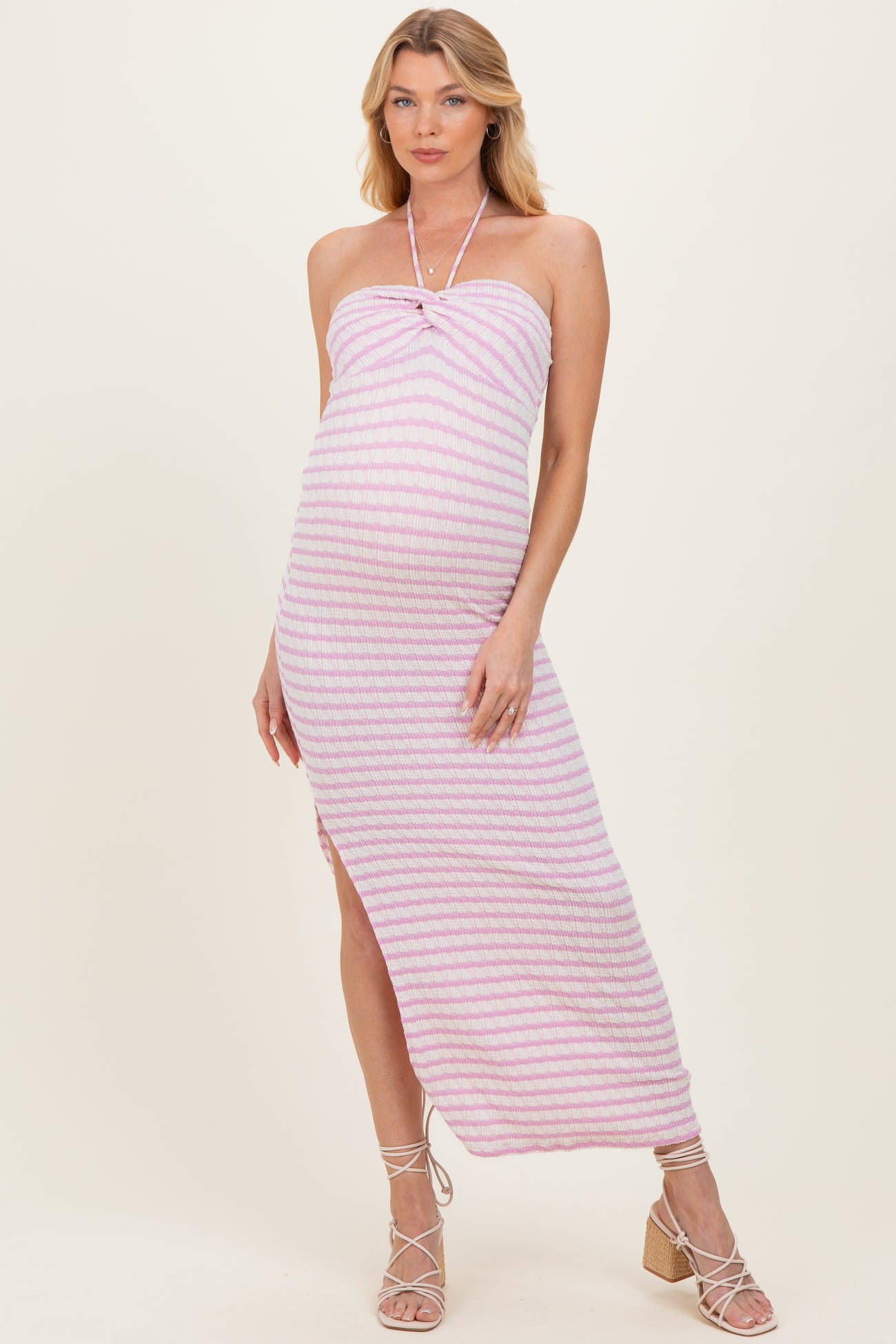 woman wearing a pink and white striped maternity maxi dress with a halter neckline and side slit, showing off her baby bump