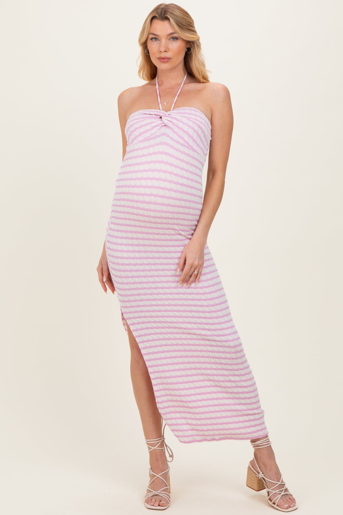 woman wearing a pink and white striped maternity maxi dress with a halter neckline and side slit, showing off her baby bump