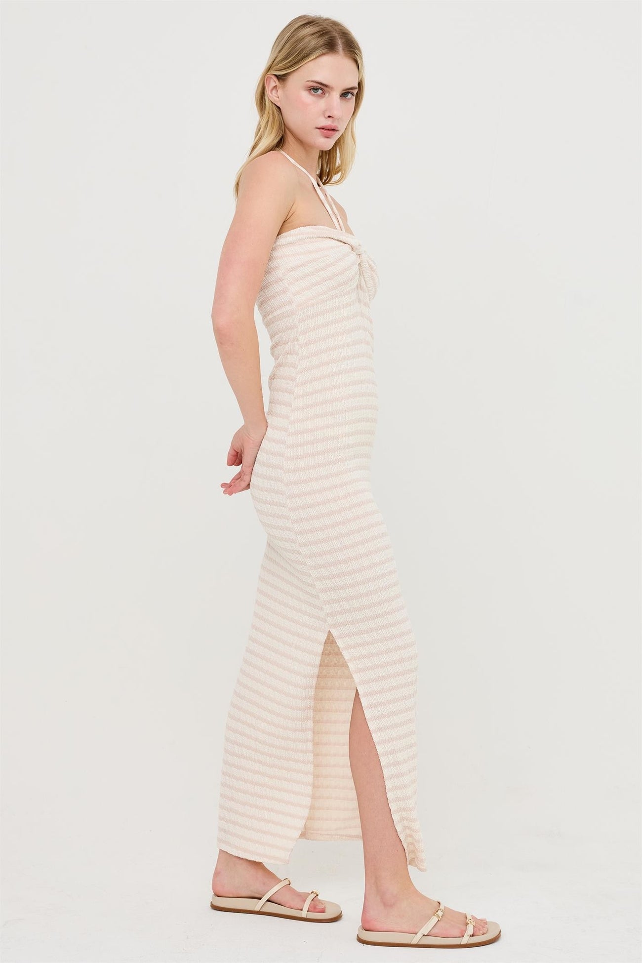 woman wearing a light pink striped maxi dress with a side slit and adjustable spaghetti straps
