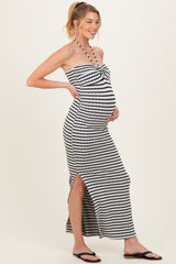woman wearing a black and white striped maternity maxi dress with a halter neck and side slit, showcasing her baby bump