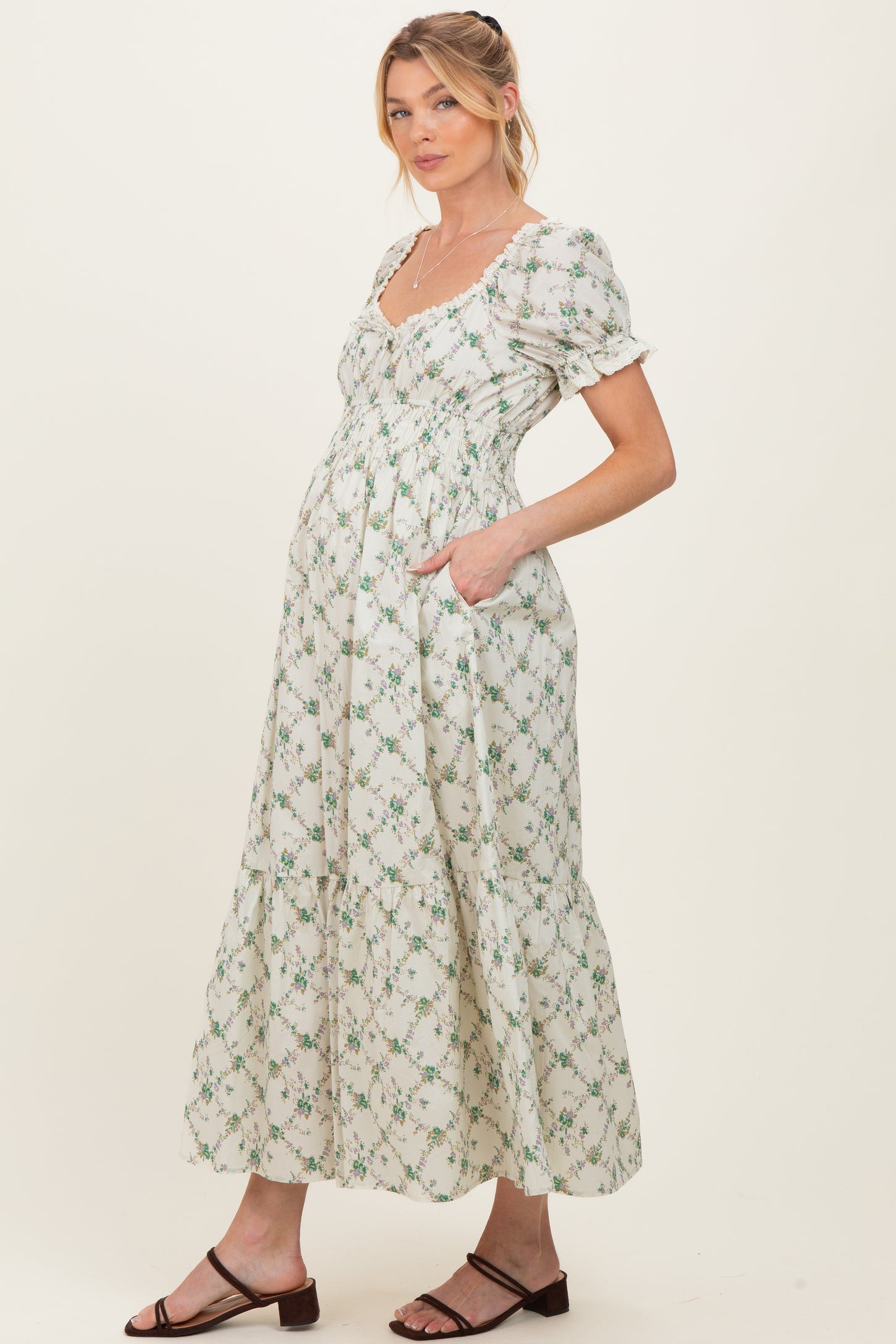 woman wearing a white floral maternity maxi dress with puff sleeves and pockets, showcasing her baby bump