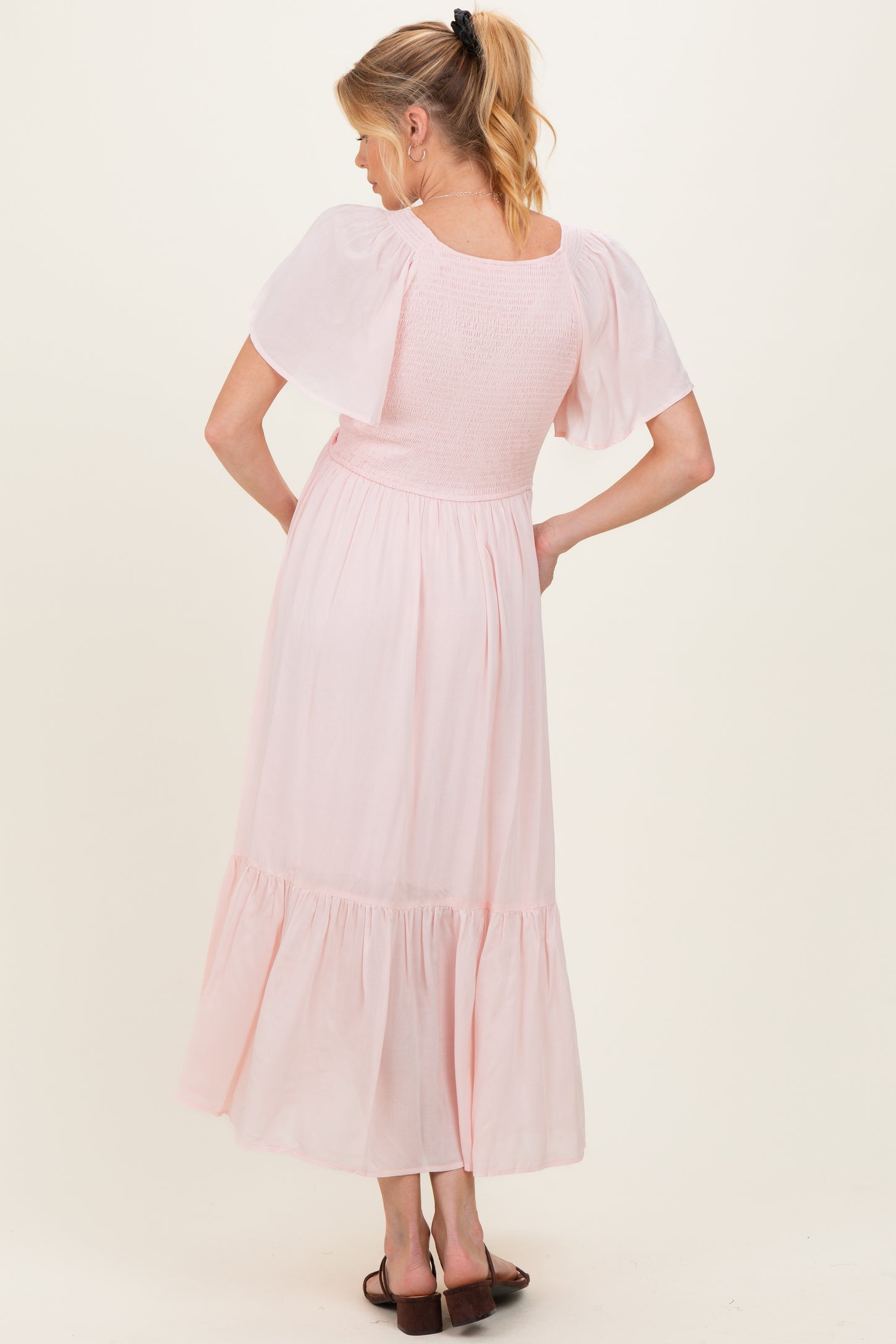 woman wearing a light pink maternity maxi dress with puff sleeves and smocked bodice, showing a baby bump from the back