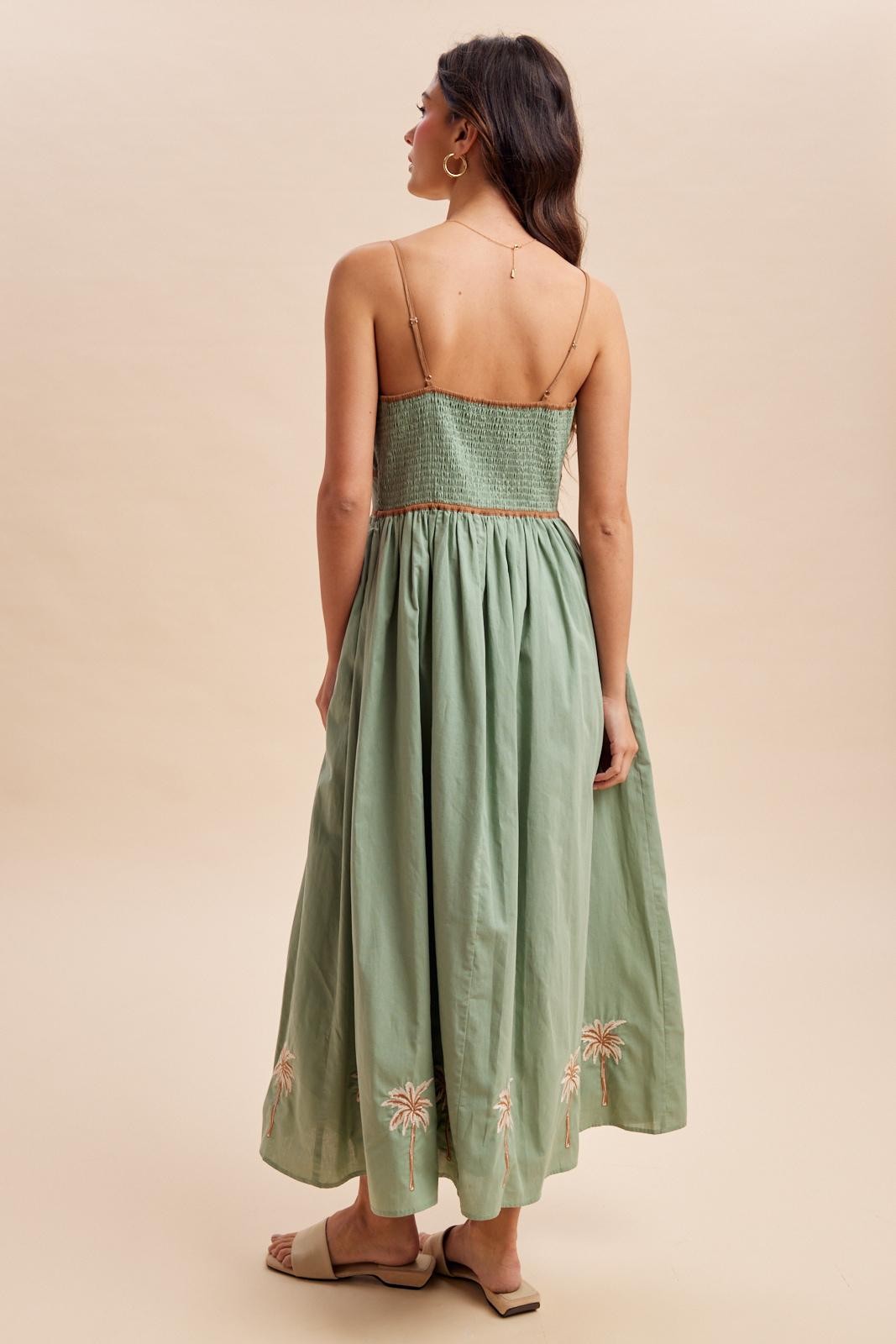 woman wearing a green maxi dress with a smocked bodice and floral embroidery at the hem, shown from the back